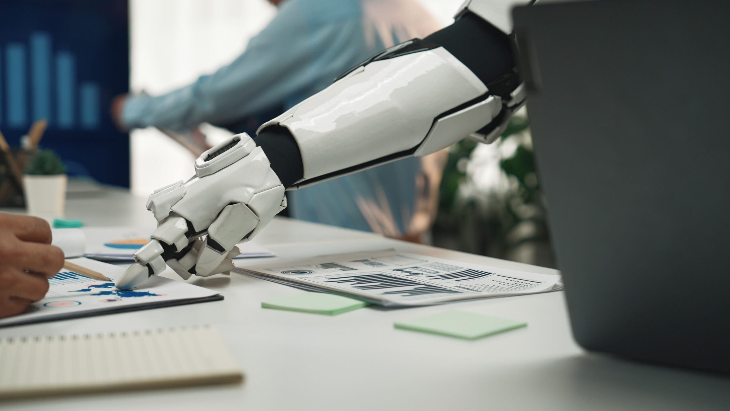 Advanced Robotic Arm Assisting Human Worker in Modern Office Environment with Financial Reports and Graphs on Table. Noogenesis